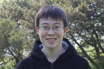 An outdoor photo of Gavin Wang wearing a black hoodie and smiling.