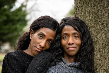 Two women pose for a portrait; one leans her head on the other's shoulder
