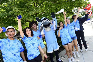 A group of student volunteers in blue tie-dye shirts pose with Jay, the mascot