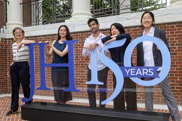 Five college students pose with a giant "JH 150 Years" sign.