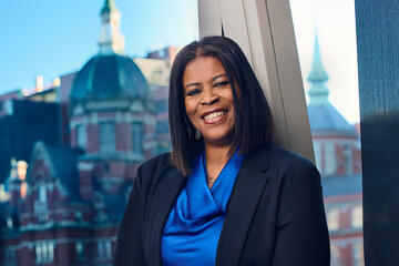 A woman in a blue blouse and black sweater poses for a photo