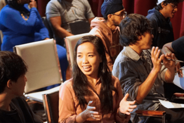 Photograph of a diverse group of people engaging with each other in conversation in an auditorium