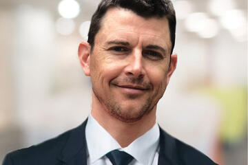 Photo of Cory Donovan, a white man in a suit with short, dark hair 