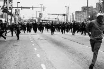 Devin Allen's black-and-white photograph of a Black man running down a street near Camden Yards away from a large group of police officers in riot gear during the 2015 Baltimore uprising following the death of Freddie Gray