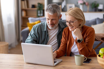 A middle-aged man and woman looking at a laptop screen together