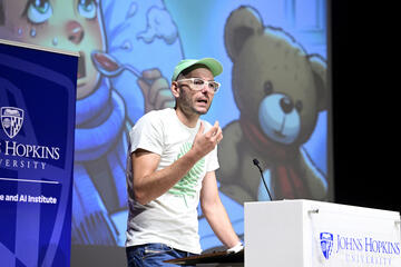 Mathias Unberath speaks on stage behind a podium in front of a screen displaying an illustration of a sick child holding a teddy bear