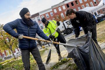 Three adults clean up a public park with shovels and trash bags.
