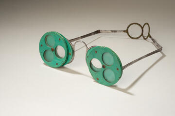 green diagnostic eyeglasses with rotating lenses. Each lens has three eye holes, each with its own shutter.