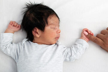 A sleeping newborn holding onto a parent's finger.