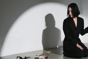 Cropped photo of Lucrecia Dalt on stage, illuminated by a spotlight, looking down toward the stage at a guitar laying down