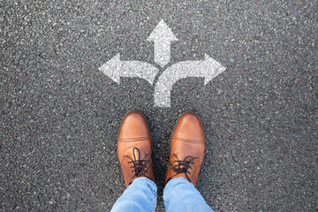 Man's feet standing on pavement in front or arrows pointing in three directions
