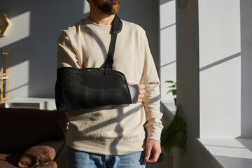 Man with arm in sling gazes out a window
