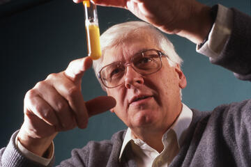 A man wearing glasses examines a test tube with a yellow liquid in it