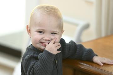 A baby smiles for the camera while standing up by leaning on a coffee table