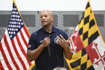 Gov. Wes Moore speaks in front of the American and Maryland flags inside the JHU ROTC building