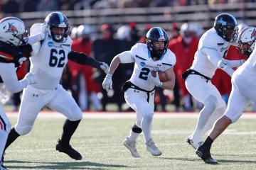 A football player in a white jersey rushes with the ball