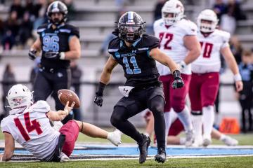 A football player in a black jersey celebrates after making a tackle