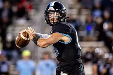 A football quarterback in a black jersey prepares to throw the ball