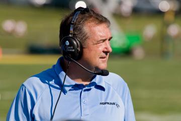 A football coach in a headset and light blue polo shirt