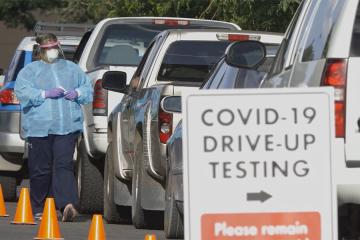 Cars queue at a sign that reads COVID-19 DRIVE-UP TESTING