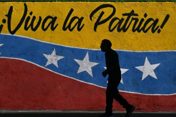 Outline of a human figure walking along a wall painted as if a mural of the Venezuelan flag with the words "&iexcl;Viva la Patria!"