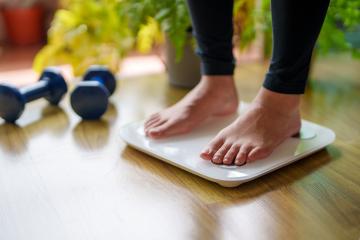 Closeup of feet on a scale. Two hand weights rest on the floor next to the scale.