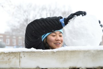 A student in a blue hat packs a snowball on top of the marble gate