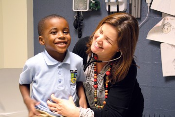 A little boy smiles while he is tickled by his doctor, who has a stethoscope in her ears