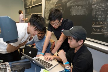 Four students huddle over a laptop