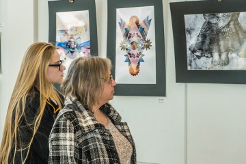 Two people look at photos mounted on the wall