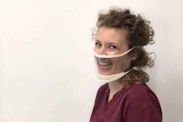 A model wears the ClearMask, and her smile is fully visible