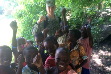 A man in military fatigues with a crowd of children