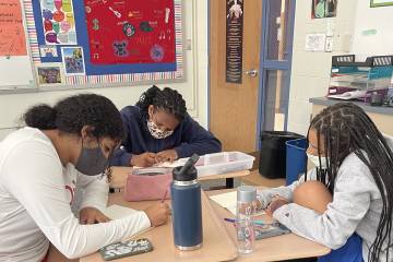 Three students at Roland Park Country School seated around a desk working on a project with Changemakers