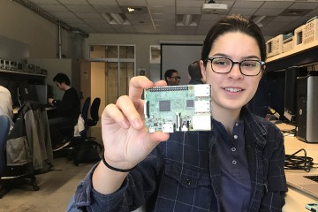 A woman holds up a small green computer chip to the camera