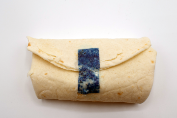 A burrito is enclosed by a strip of tape that has been dyed blue to illustrate its use
