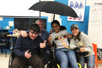 Members of team Rain Rain Go Away pose with their invention and a man who uses a wheelchair