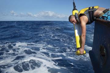 A man hangs over the edge of a boat, deploying an Argo float into the ocean
