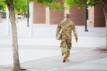 A student in a military uniform walks across a college campus