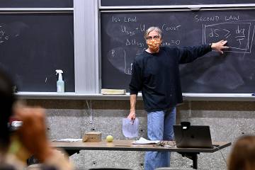 Biophysical Chemistry Professor Doug Barrick, wearing a mask, stands by a blackboard in front of his class