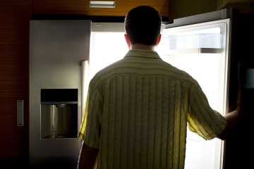 Man is silhouetted as he stands in front of open refrigerator door