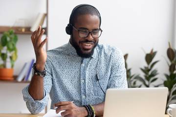 Smiling man in headphones engaged with instructor on laptop