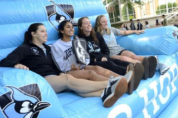 Four students sit in an inflatable chair holding a Blue Jay shield 