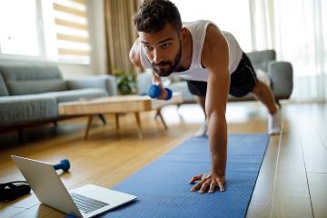 Man exercizing in his living room while looking at his laptop screen