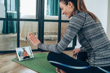 Woman on yoga mat waving to woman in same pose on a video screen