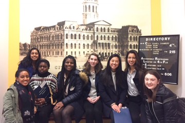 A group of 8 students pose for a photo in front of an image of City Hall