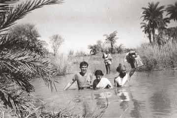 Black and white image features Carl Taylor and three guides crossing a deep river in India