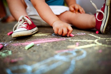 Young child colors on sidewalk with chalk