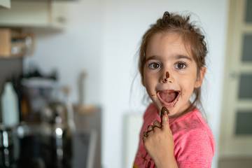 Girl eating chocolate frosting with her finger