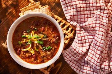 a bowl of chili with scallions, cheddar cheese, and crackers