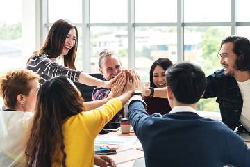 Group of multiethnic diverse people high-five, laughing and smiling together in a meeting in the office